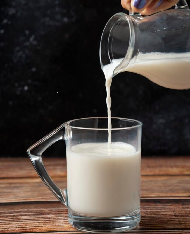 Woman pouring milk into the glass mug wooden table