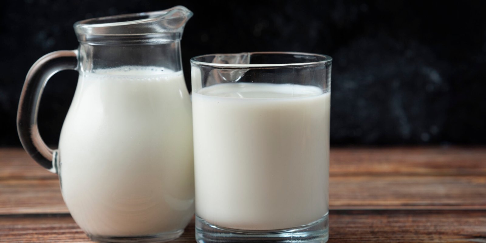 Fresh milk in a mug and jug on wooden table