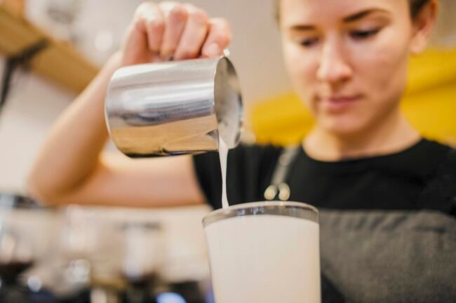 low-angle-barista-pouring-milk-glass